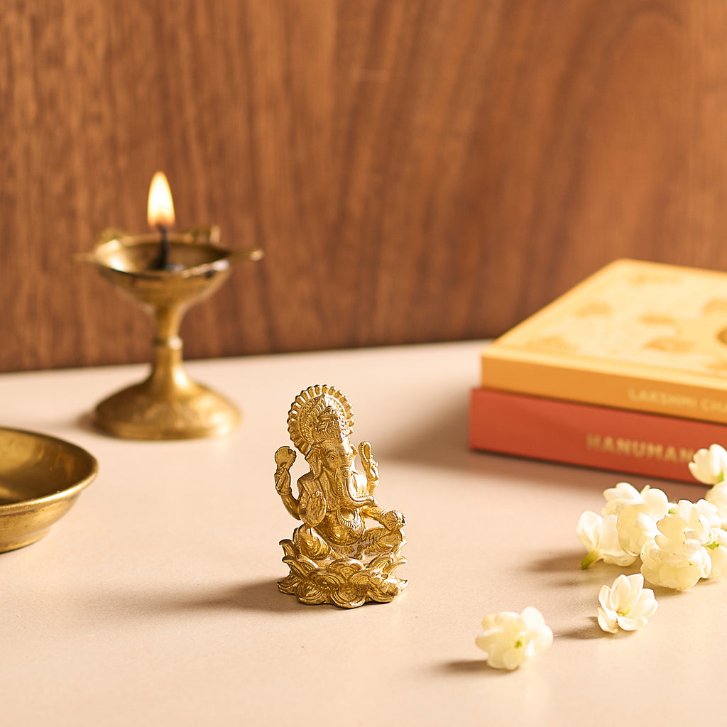 Gold statue of a deity on a table with a lit candle and books in the background