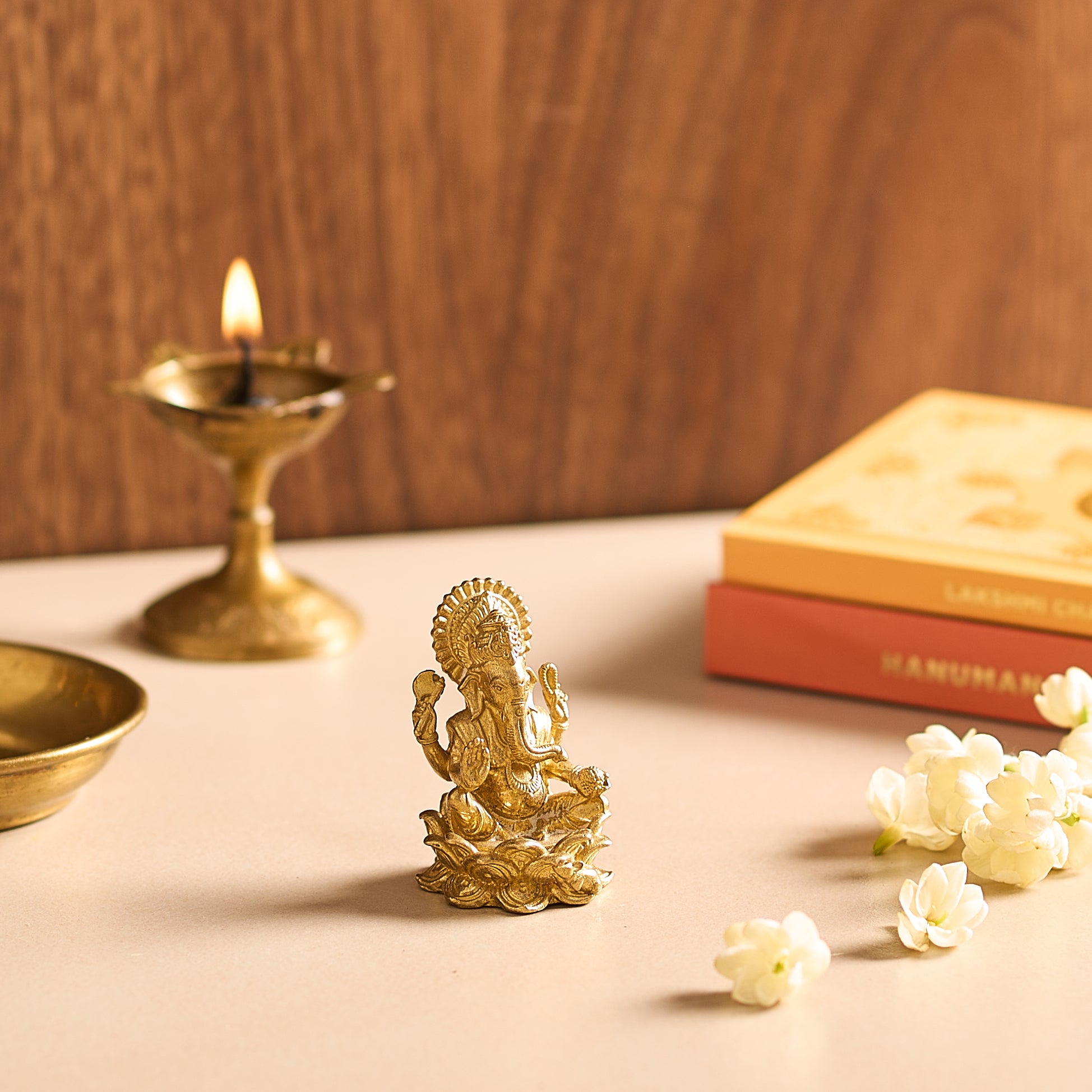 Gold statue of a deity on a table with a lit candle and books in the background