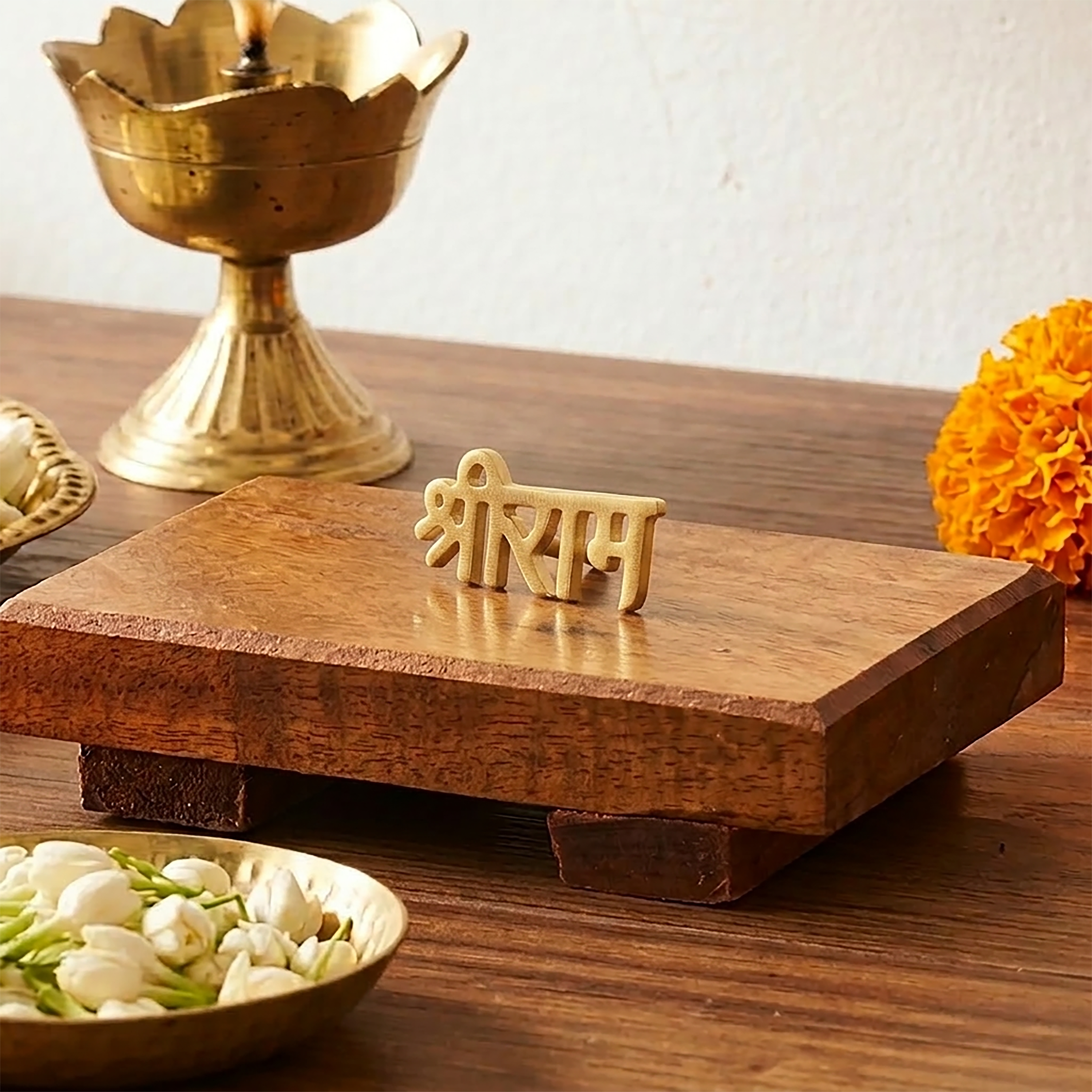 Brass 'Aum' symbol on a wooden platform with flowers and a bowl on a wooden surface.