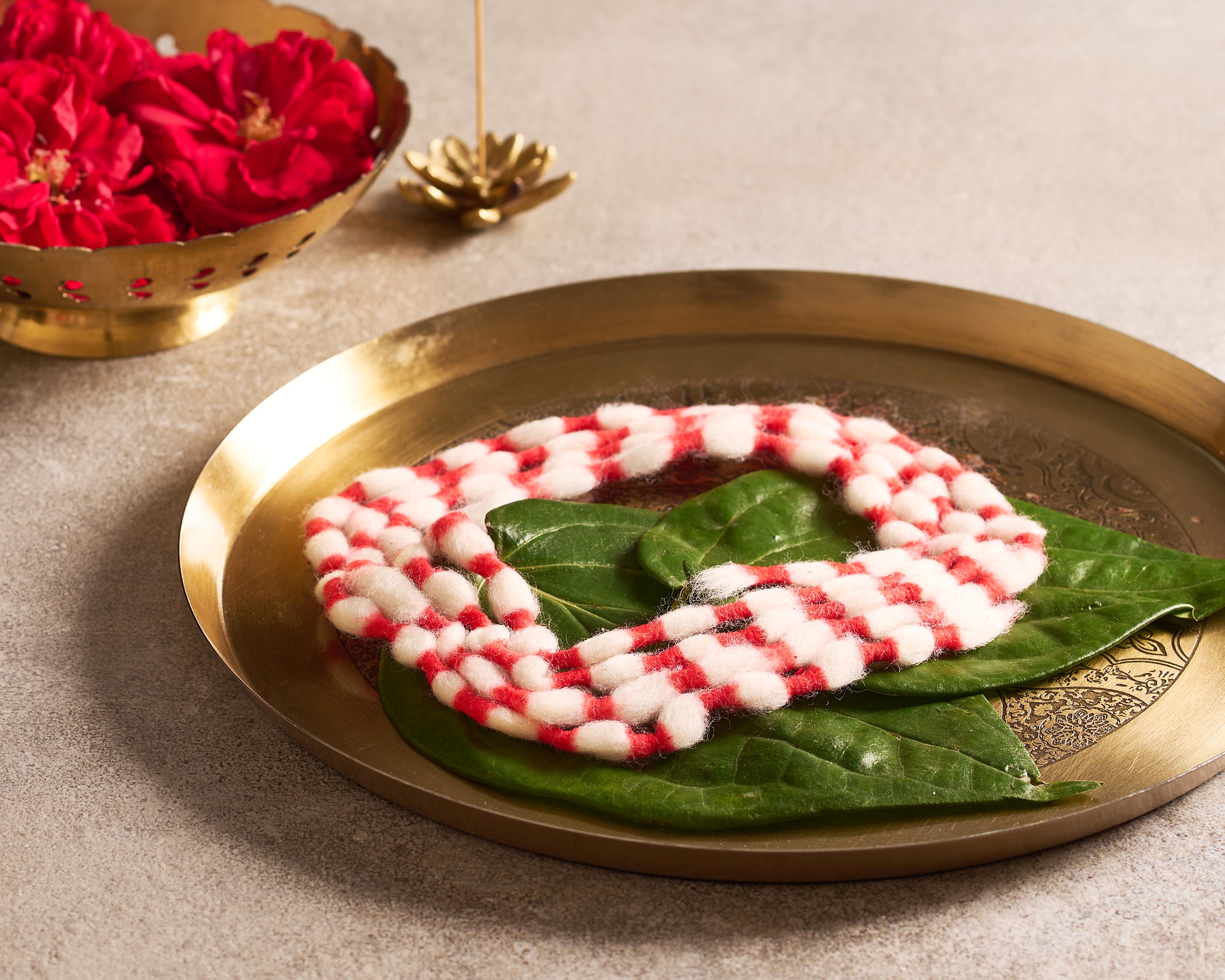 Decorative red and white pattern on a green leaf on a gold plate with flowers in the background