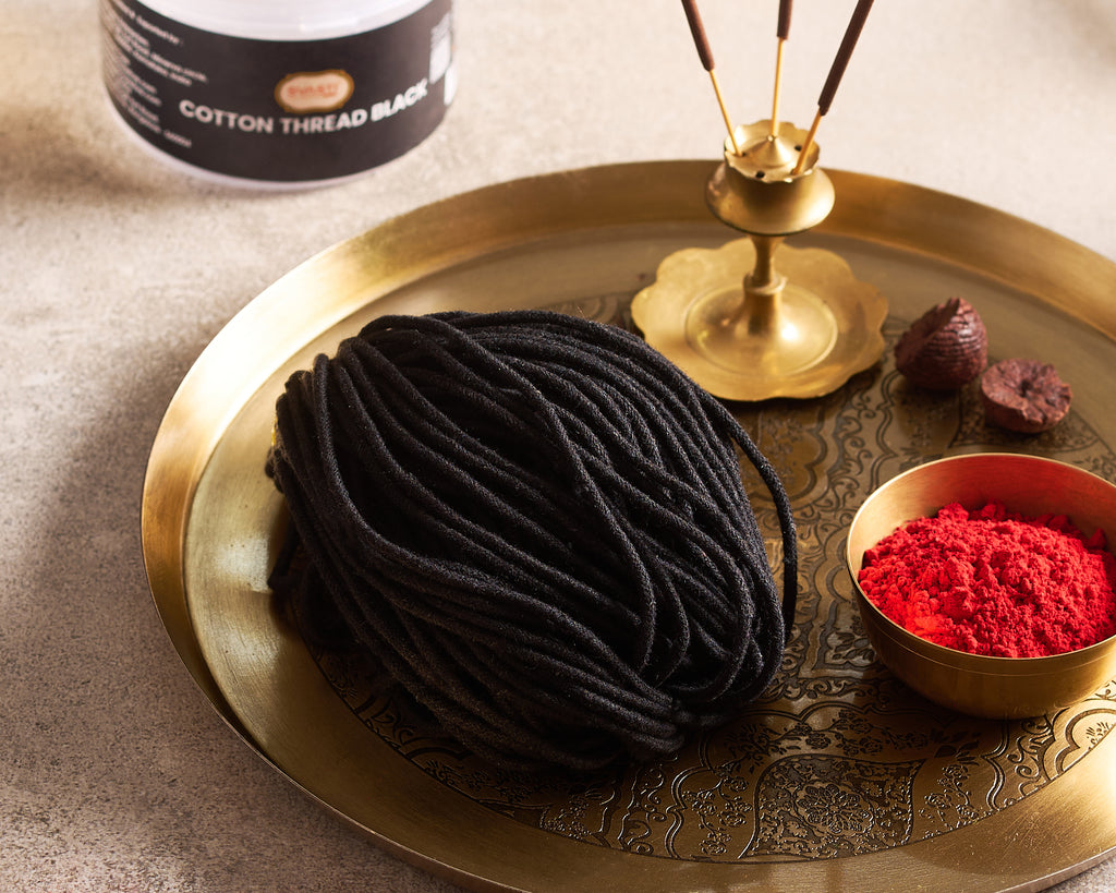 Black cotton thread on a gold tray with red powder and a bottle of cotton thread.