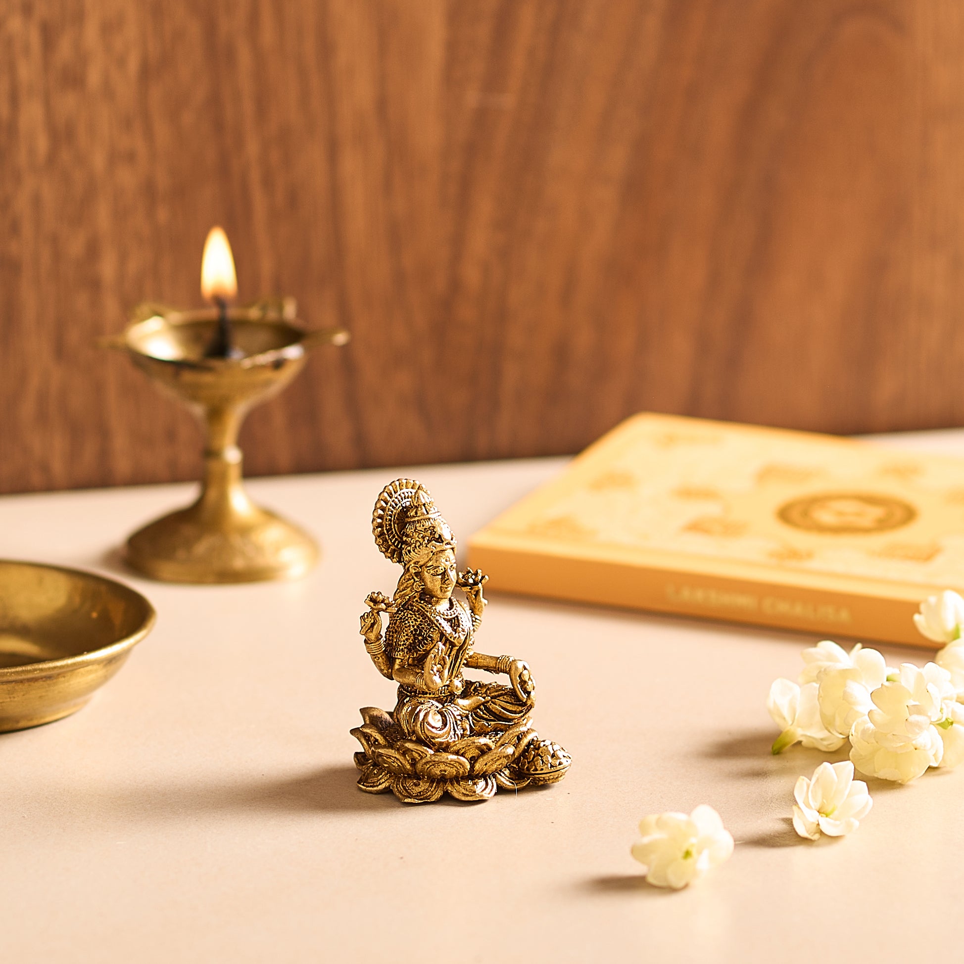 Gold statue of a deity on a table with a lit candle and flowers