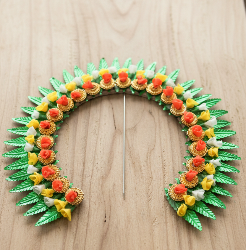 A handmade U-shaped necklace or hair ornament made of green leaf-shaped beads, gold-toned circular beads, and small orange, yellow, and white flower-like accents, displayed on a light wood surface.