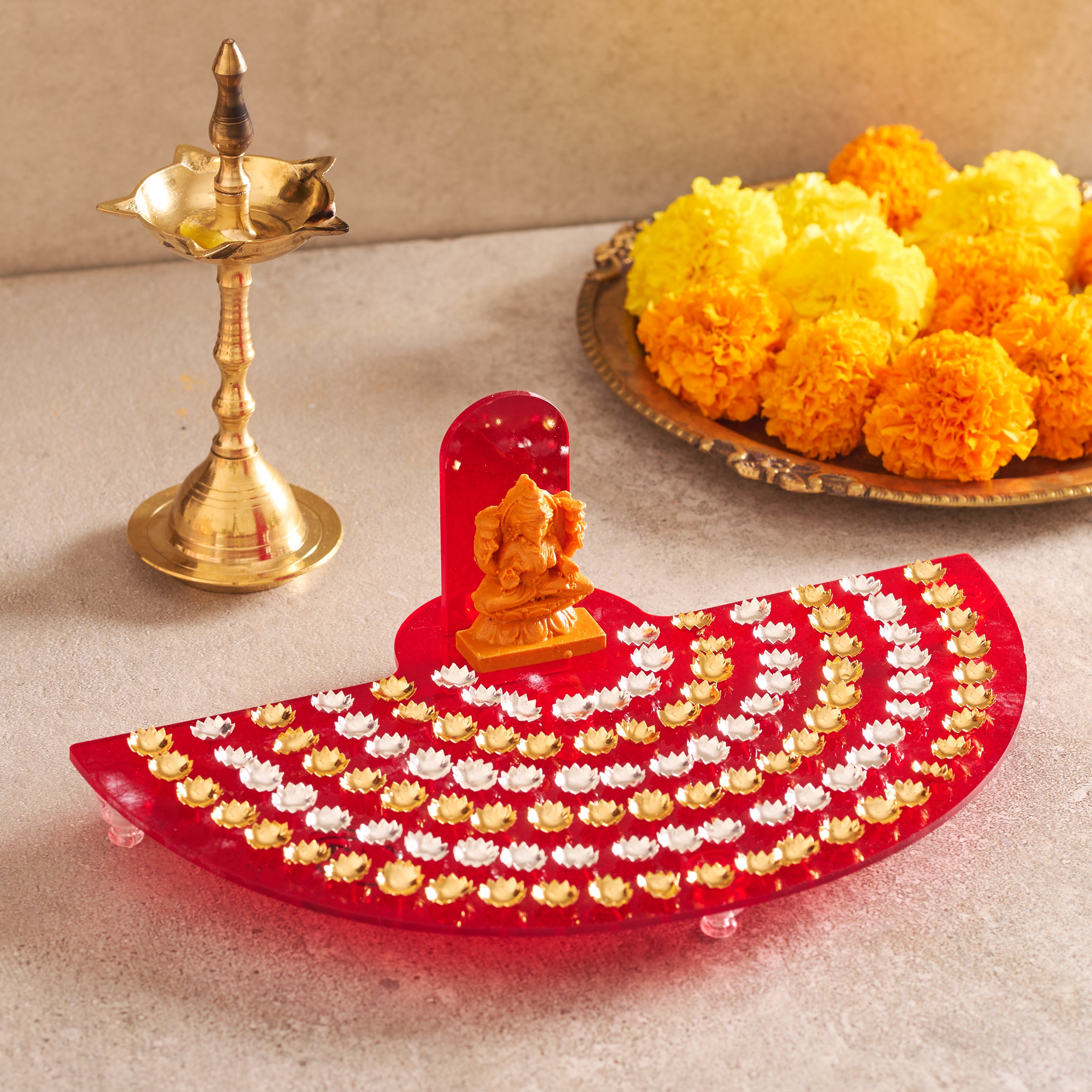 Decorative diya with Lord Ganesha, marigold flowers, and a brass lamp on a light background