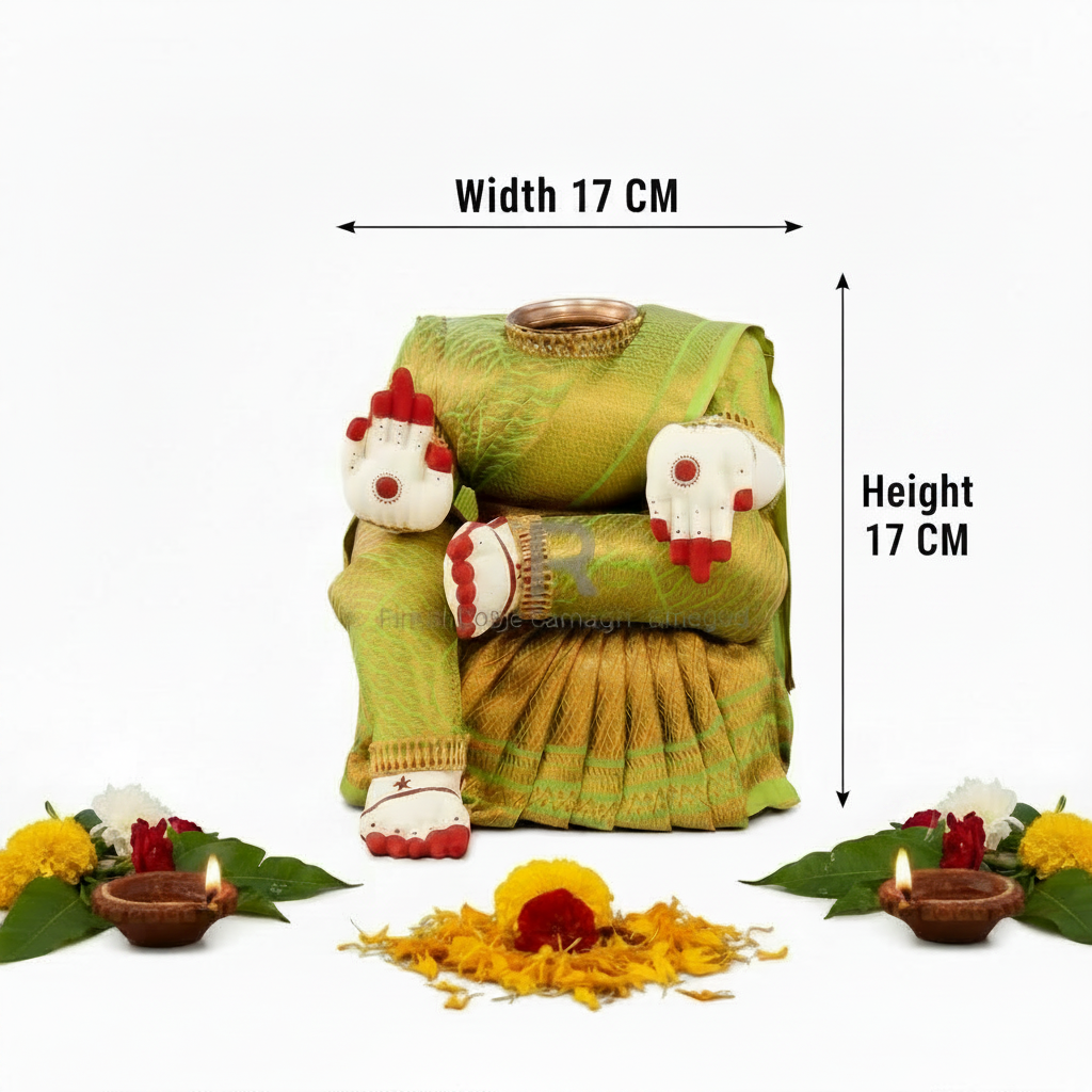 A folded green and gold saree displayed on a mannequin form, surrounded by decorative props including marigold petals, small clay lamps, flowers, and white decorative figures with red details, all on a plain white background.