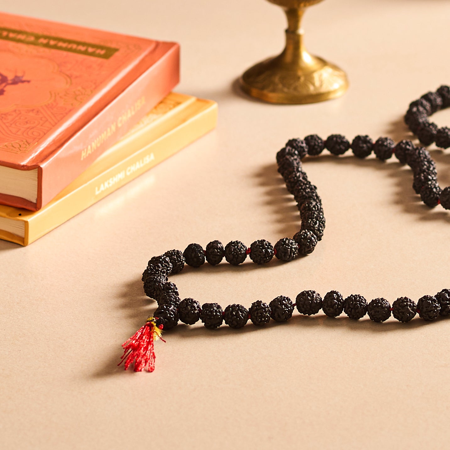 Black beaded necklace with a red tassel on a beige surface with books and a candle.