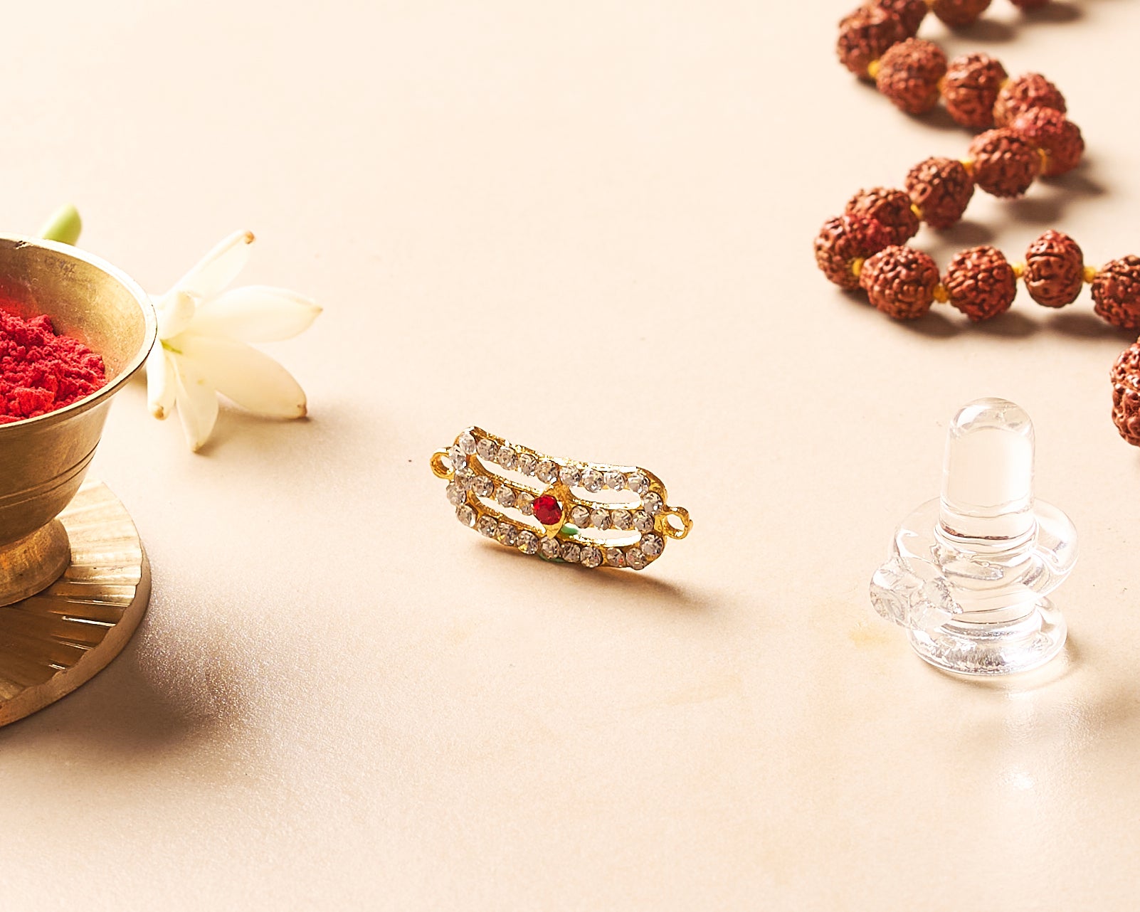 Gold ring with red stone, clear crystal object, and rudraksha beads on a light surface