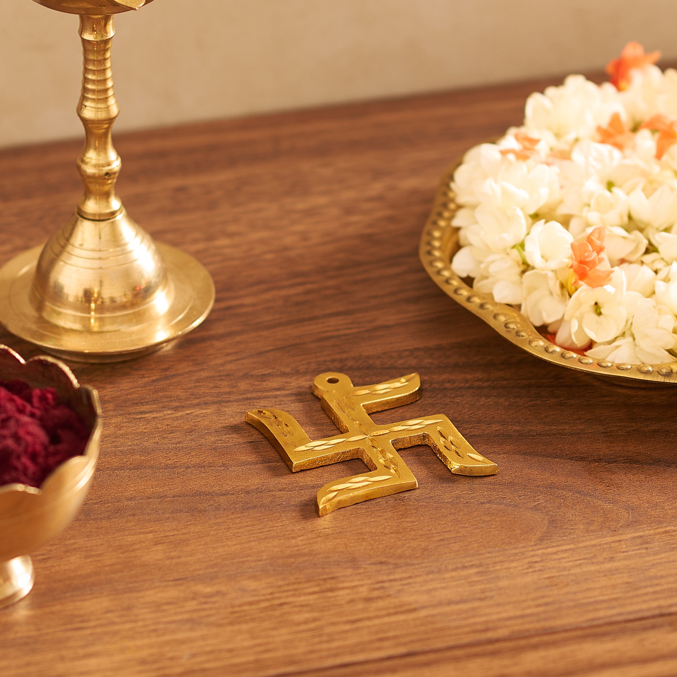 As seen in Brass Vastu Swastik_04175.jpg, a direct top-down view of the golden brass swastik is resting flat on a rich wooden grain table, showcasing its symmetrical structure and textured etchings.