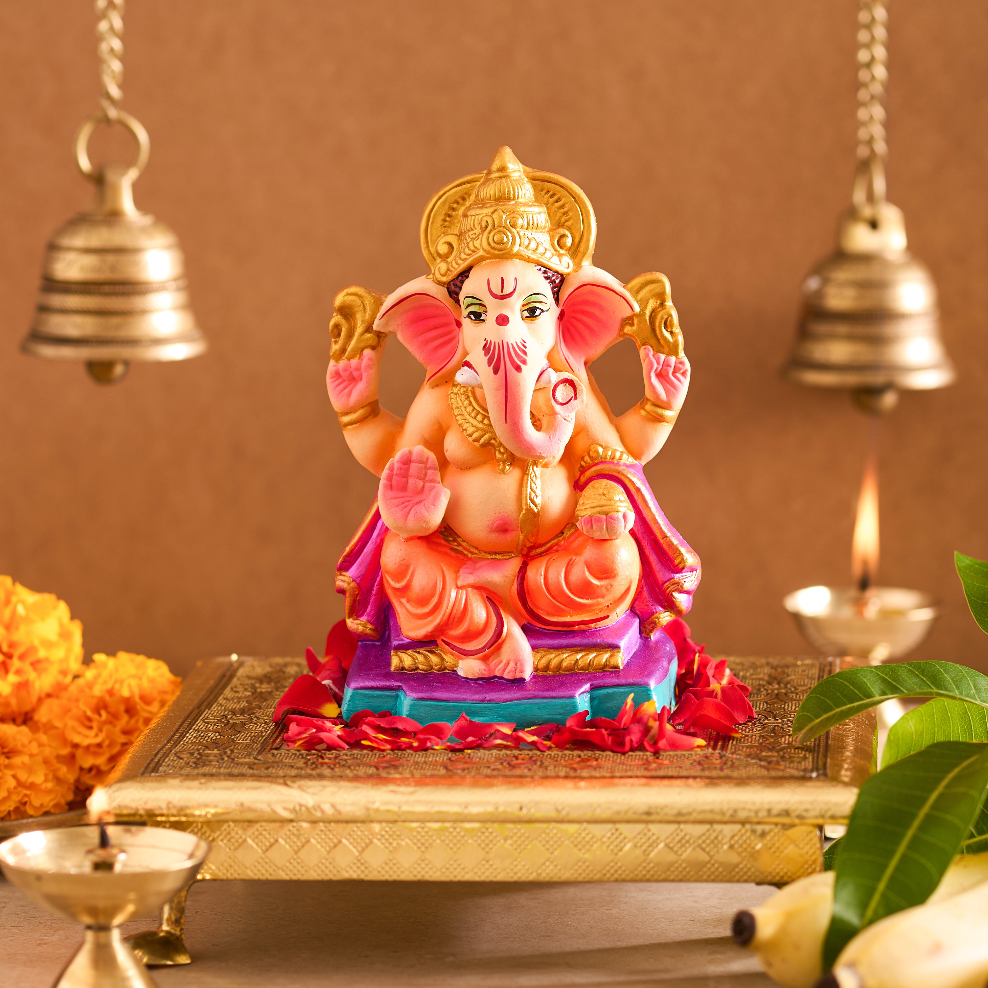 Colorful statue of a deity on a decorative platform with bells and flowers in the background.