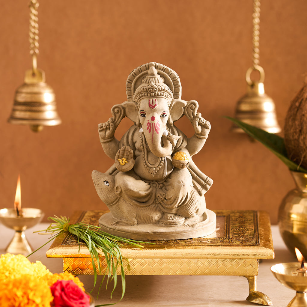 Front view of the matte grey clay Ganesha idol showing hand-painted red accents and a gold modak on an altar setup.