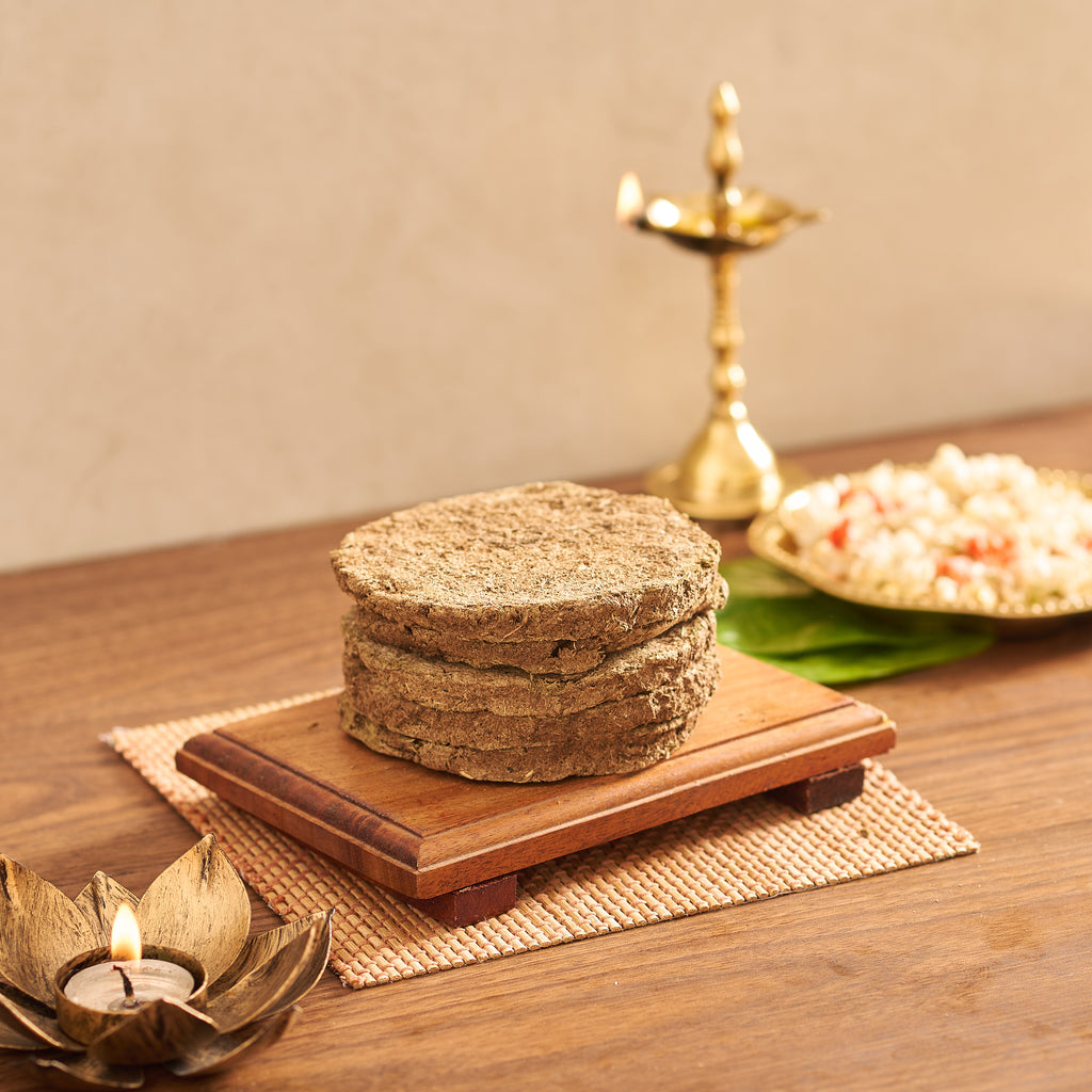 As seen in Cow Dung Cake_04338.jpg, a stack of five circular, textured brown cow dung cakes resting flat on a rectangular wooden board setup.