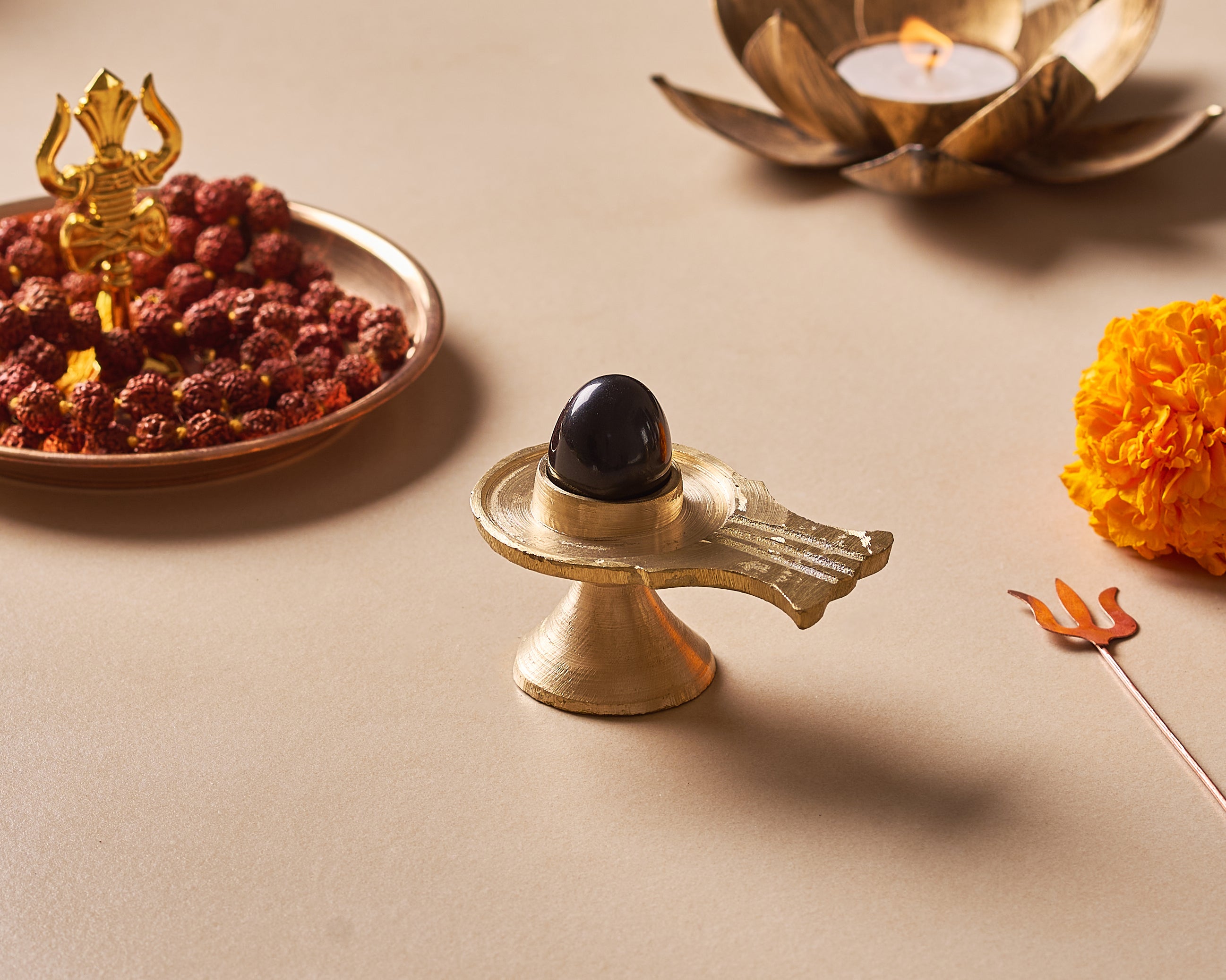 Brass Shiva Lingam with black stone on a beige surface, surrounded by religious items.