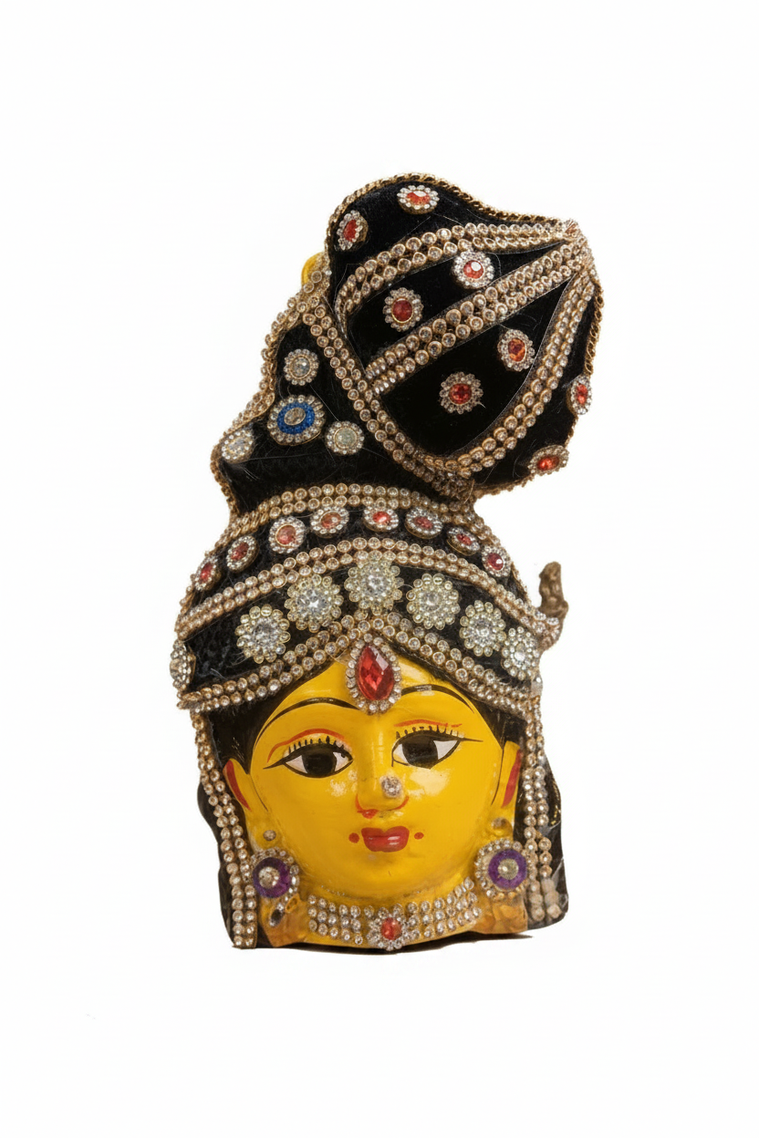 A decorative figurine of a stylized face with a bright yellow complexion, black hair, and elaborate jeweled headwear and jewelry, photographed against a plain warm beige background.