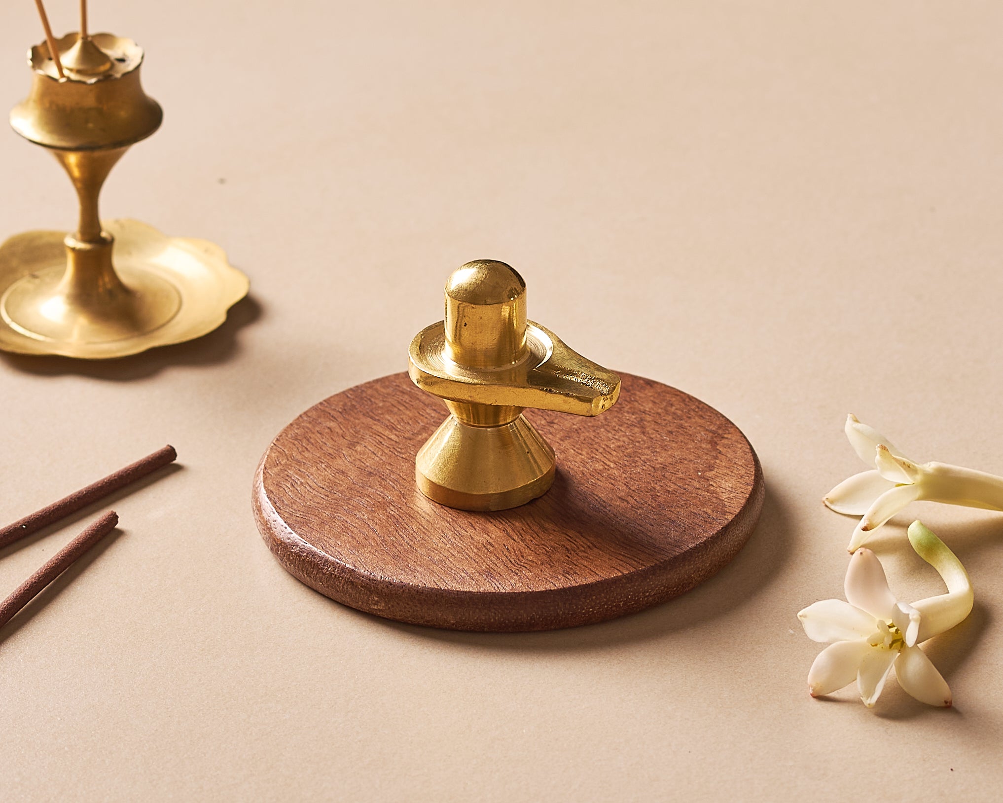 Brass Shiva Lingam on a wooden base with flowers and incense on a beige background