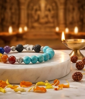 Colorful beaded bracelet on a pedestal with decorative items including a kalash and diya, set against a warm, candlelit background.