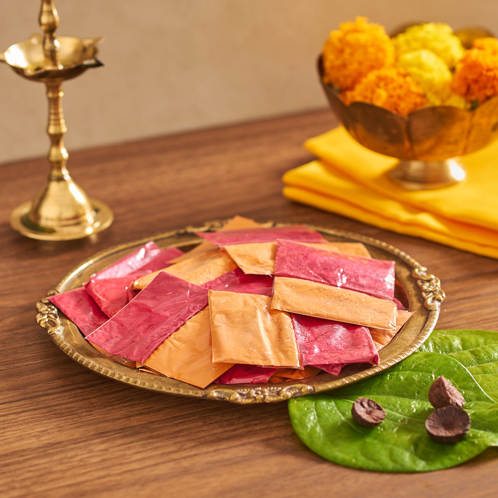 Decorative tray with pink and orange items on a wooden table with flowers and a lamp in the background.