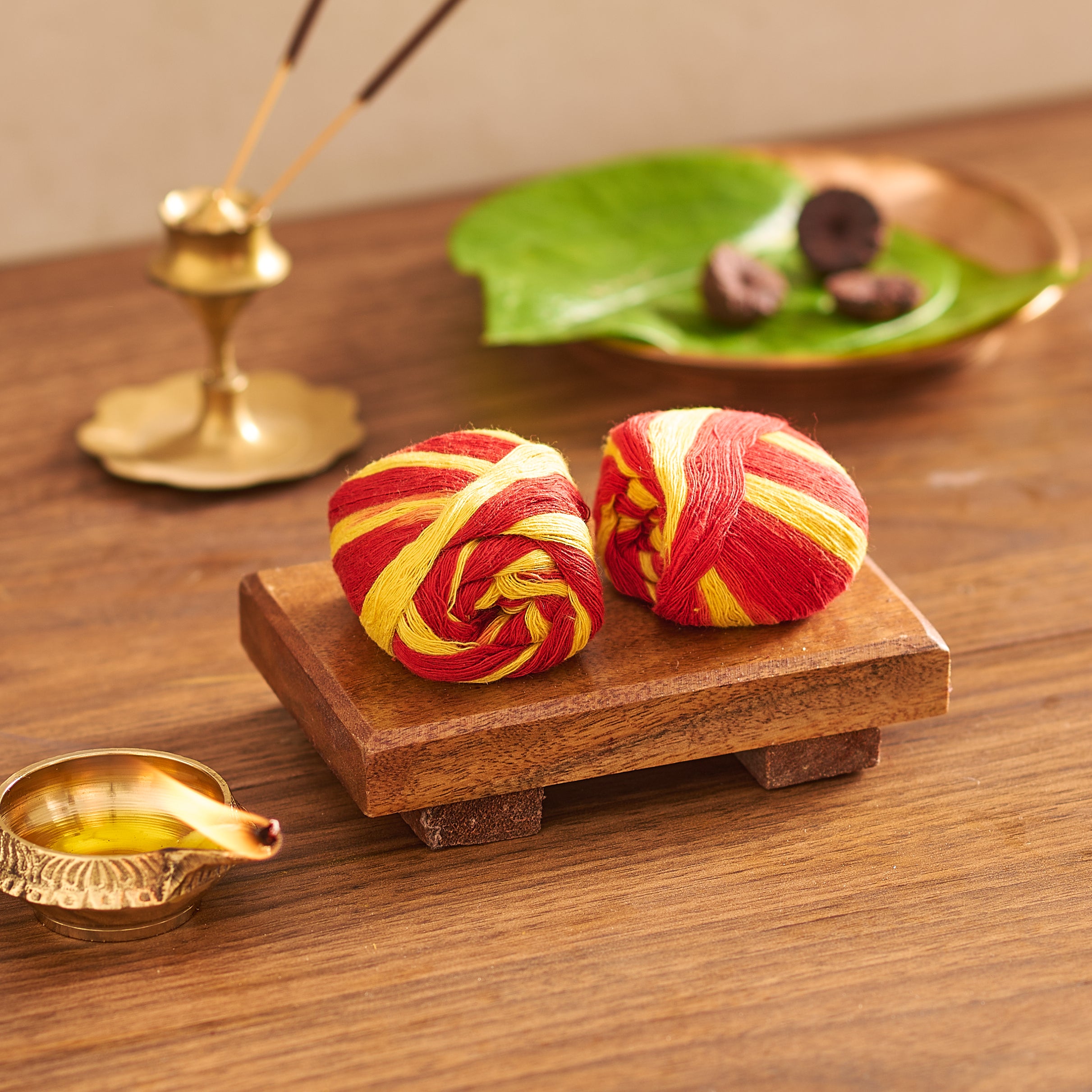 Two red and yellow striped items on a wooden platform with incense and leaves in the background.