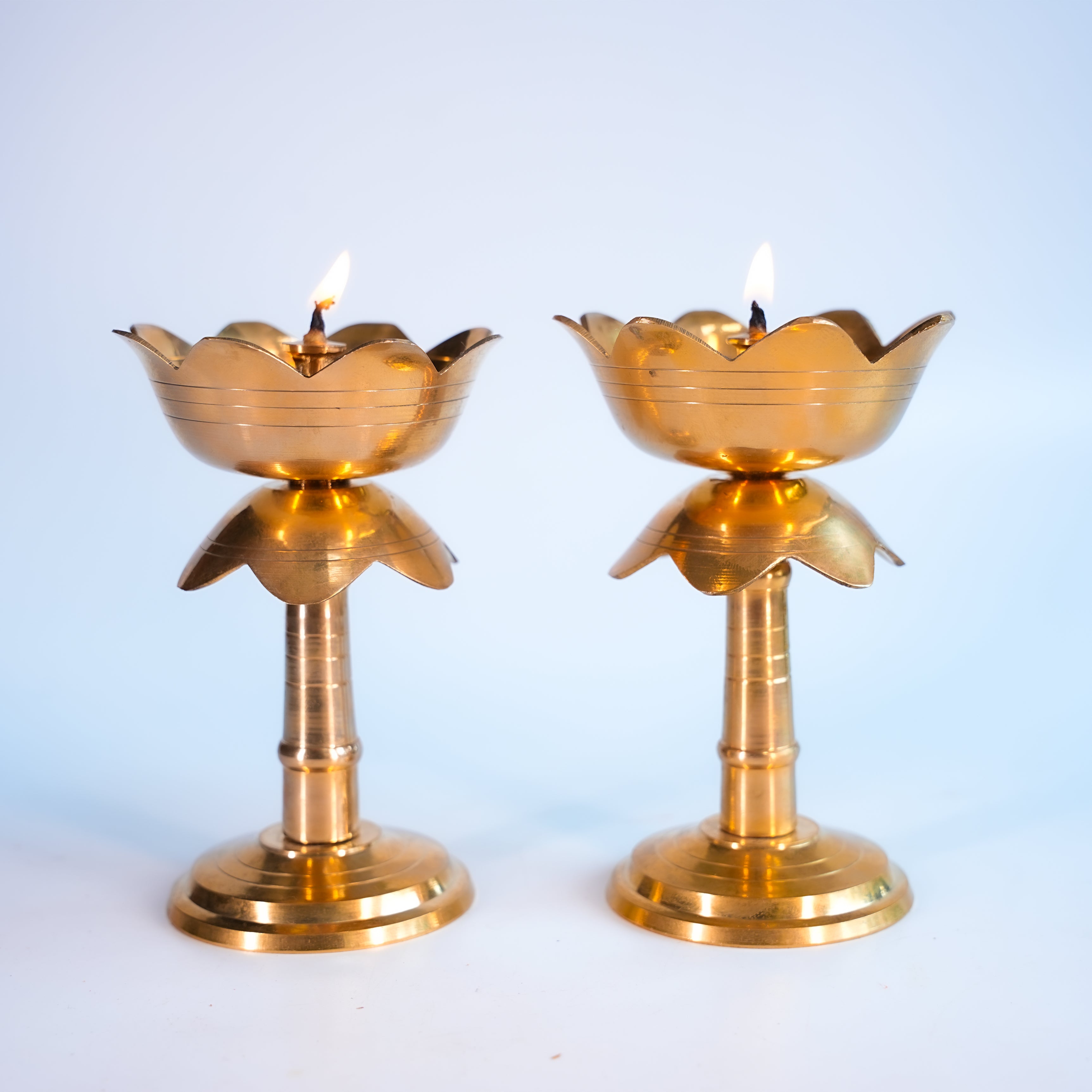 Two brass lotus-shaped candle holders with lit candles on a light blue background