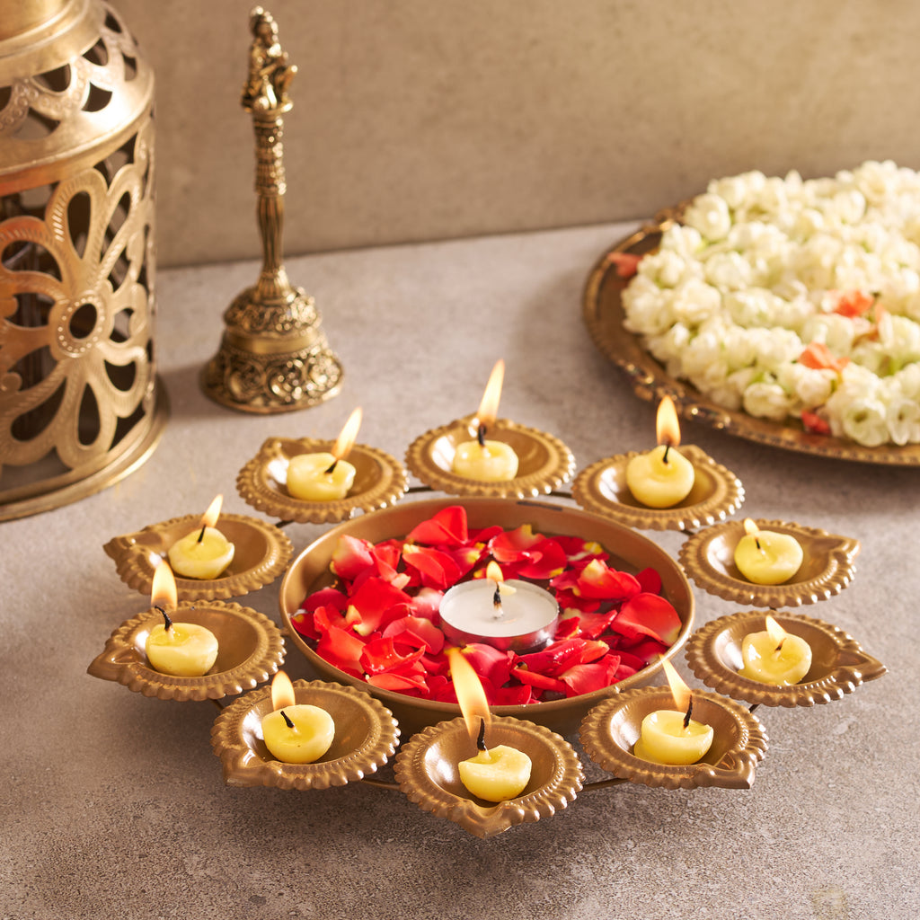 Decorative setup with lit candles, flowers, and a bell on a table.