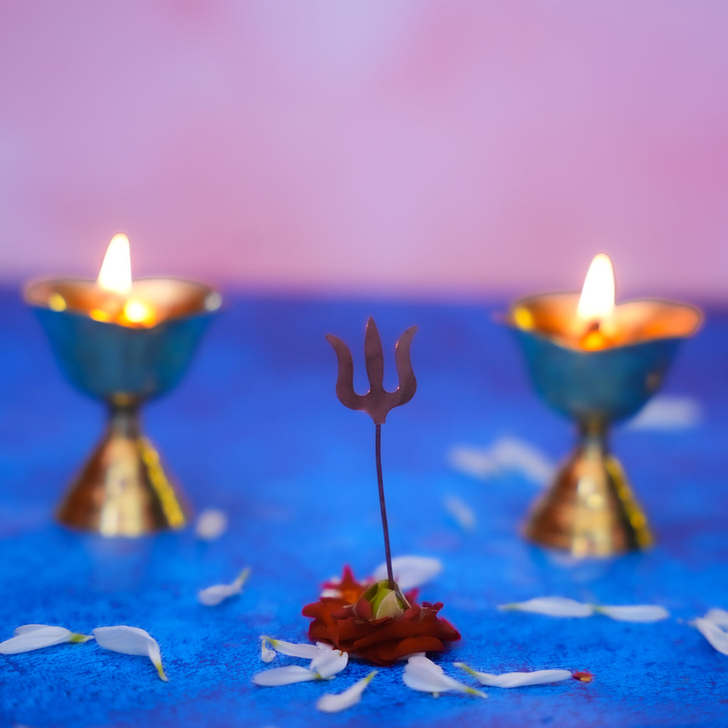 Decorative trident with flowers on a blue surface with two lit candles in the background.