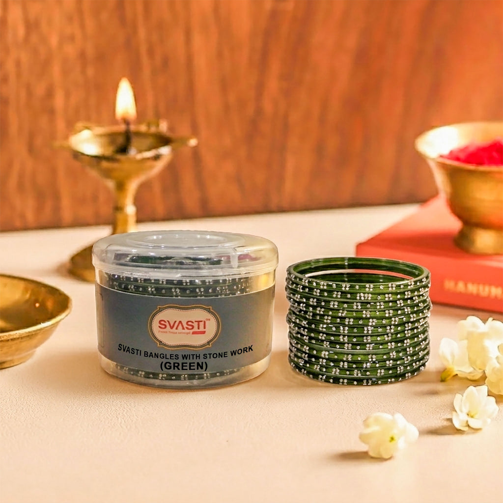 Green bangles with stone work in a container on a table with a candle and flowers.