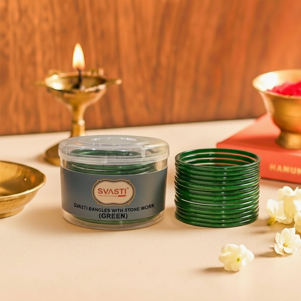Green bangles with stone work in a container on a table with a candle and flowers.