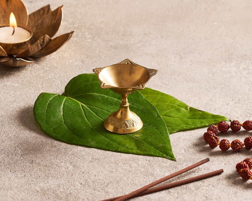 Brass lamp on a green leaf with a candle and beads on a neutral background