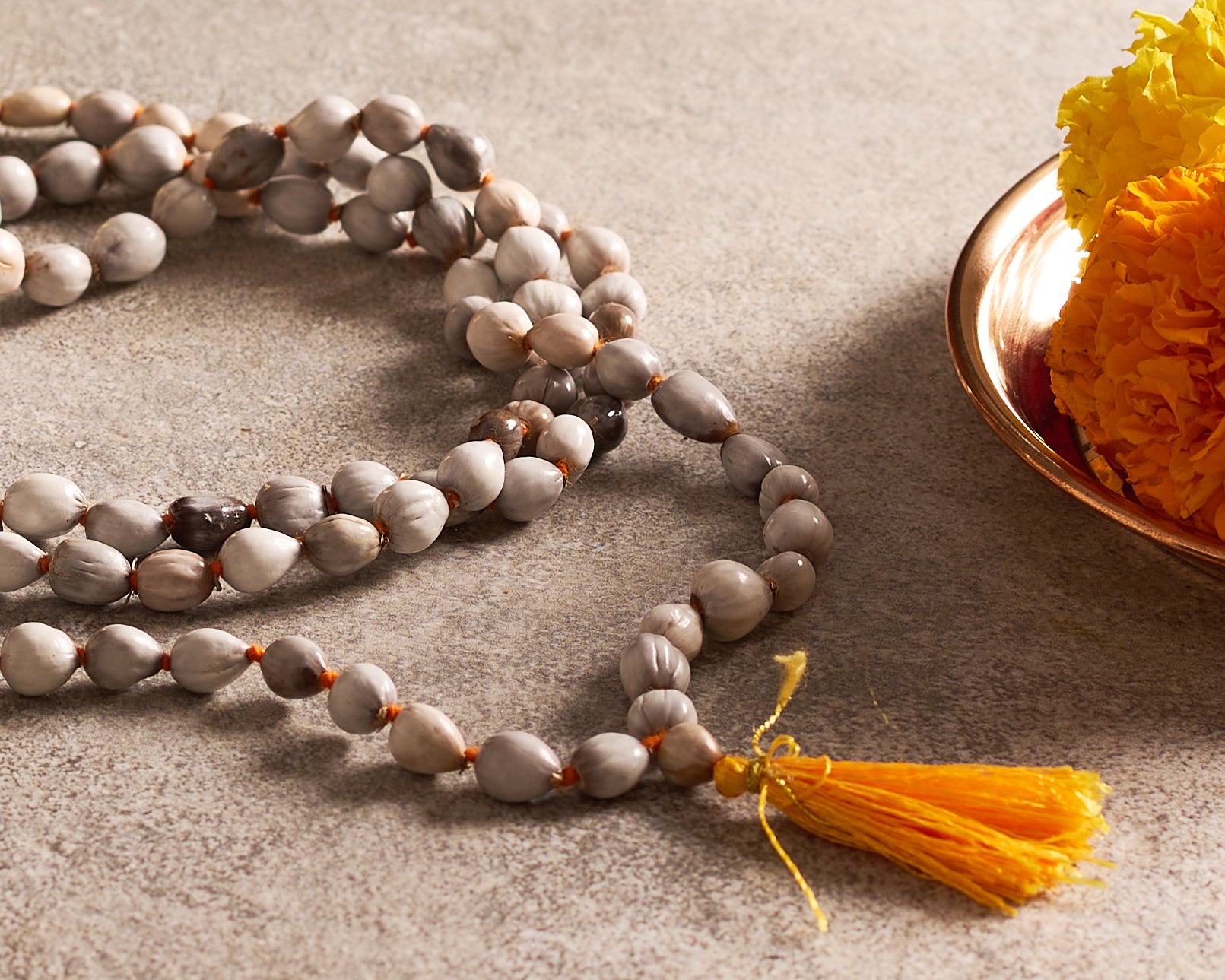 Meditation beads with a yellow tassel on a textured surface