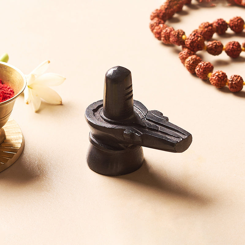 Black metal Shiva lingam on a light surface with flowers and beads in the background
