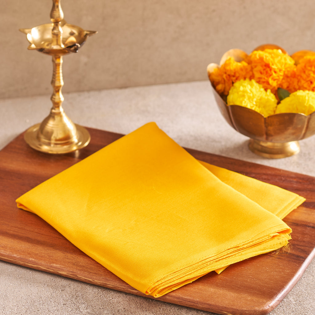 As seen in Copy of Yellow Cloth_04107.jpg, a neatly folded rectangular turmeric-yellow cotton cloth resting flat on a polished dark wood rectangular platter.