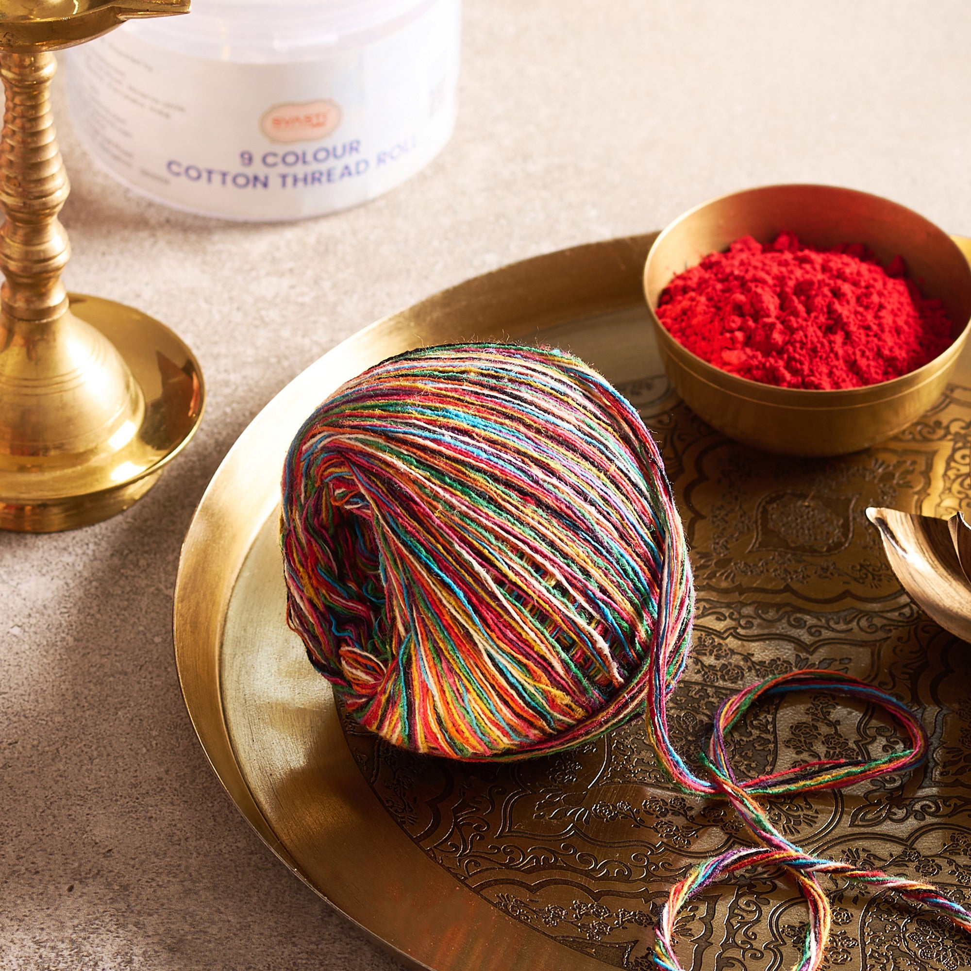 Multicolored yarn ball on a decorative tray with a bowl of red thread in the background.