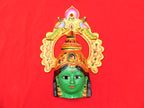 A decorative aluminum item featuring the face of Ashta Lakshmi, the Hindu goddess of wealth, with a vibrant green complexion and gold details against a red background.